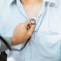 Doctor listening to cheerful young patients chest with stethoscope in his office at the hospital.